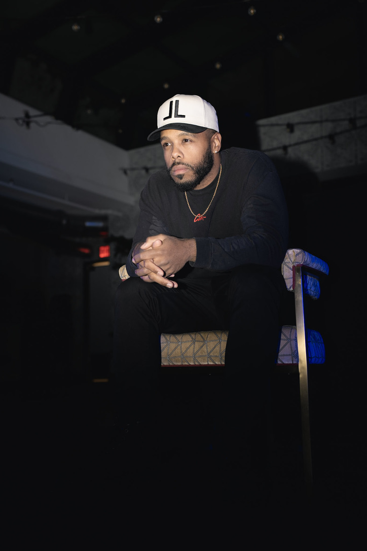 Portrait of Rolando “Roe” Ruiz seated in low light, hands clasped